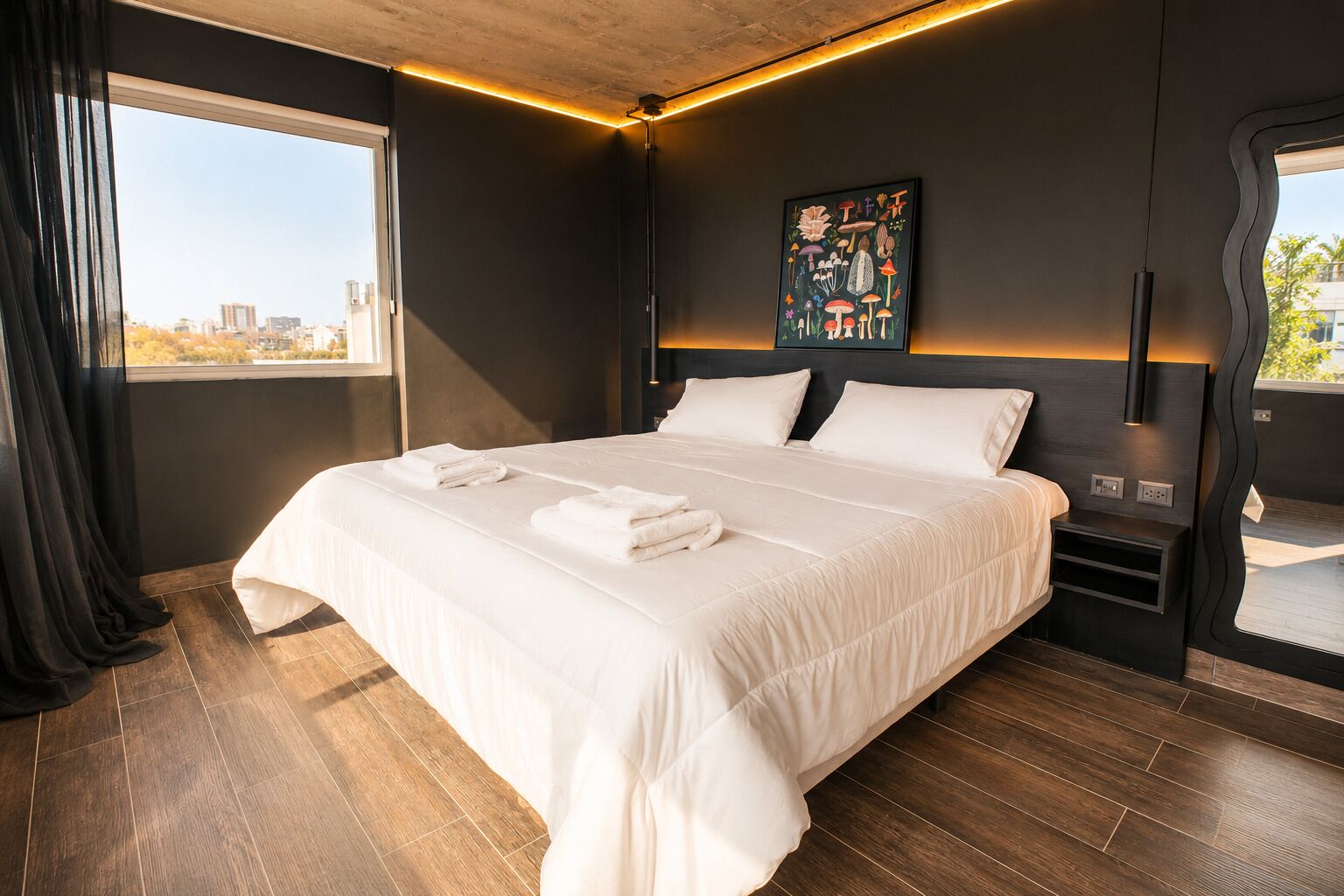 A modern hotel room with a large bed, a city view, and a unique wall art piece.