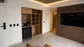 Una sala de estar moderna con televisor empotrado, estantería de madera y una pequeña cocina.