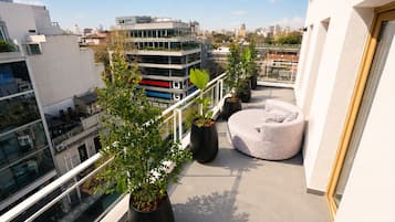 Un balcón con plantas en macetas, un espacio de estar circular y vistas a la ciudad.