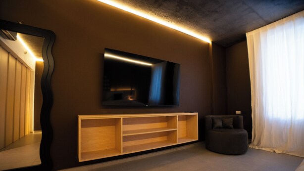 Ein modernes Wohnzimmer mit einem an der Wand befestigten Flachbildfernseher, einer Holz-Unterhaltungseinheit darunter und einem dunkelgrauen Sofa.