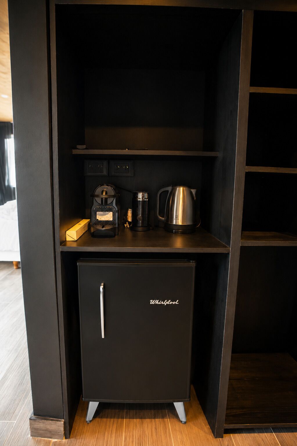 A compact kitchen area with a Whirlpool refrigerator, a coffee maker, and a kettle on the countertop.