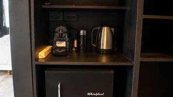 Un espace cuisine compact comprenant un réfrigérateur Whirlpool, une machine à café et une bouilloire posés sur le plan de travail.