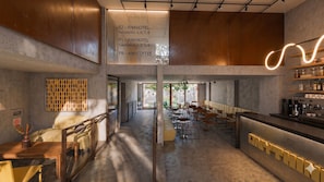 Un interior moderno con una barra central, diferentes disposiciones de asientos y un letrero que indica la ubicación de las habitaciones y el café.