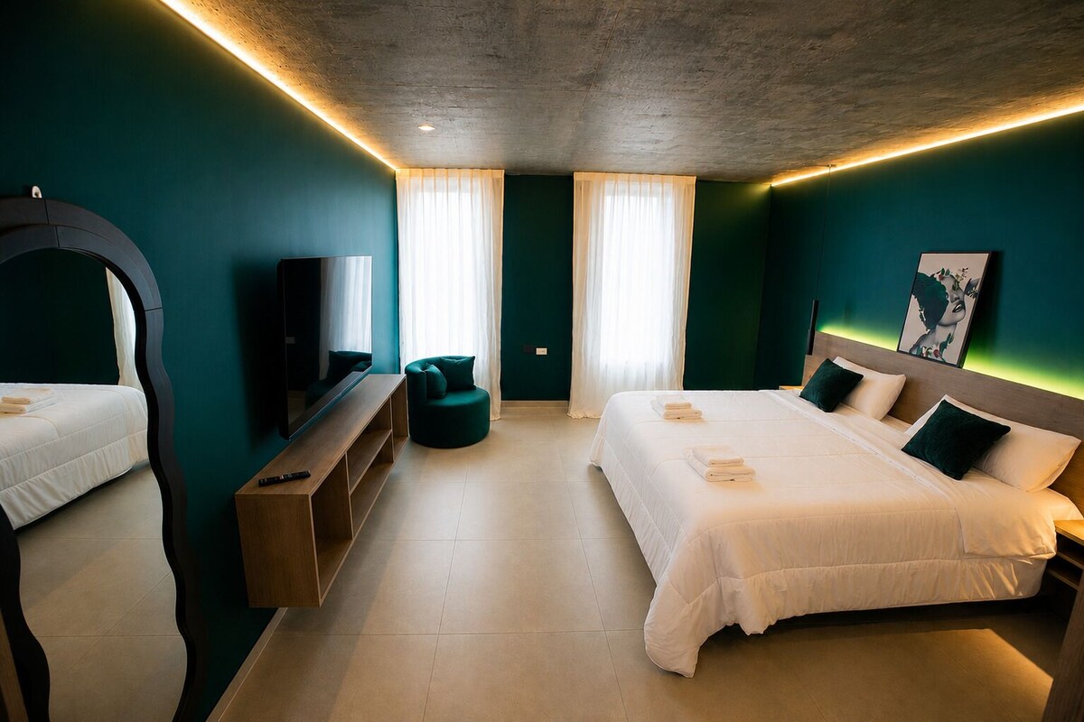 Habitación de hotel con dos camas, televisión, zona de estar y ventana grande.