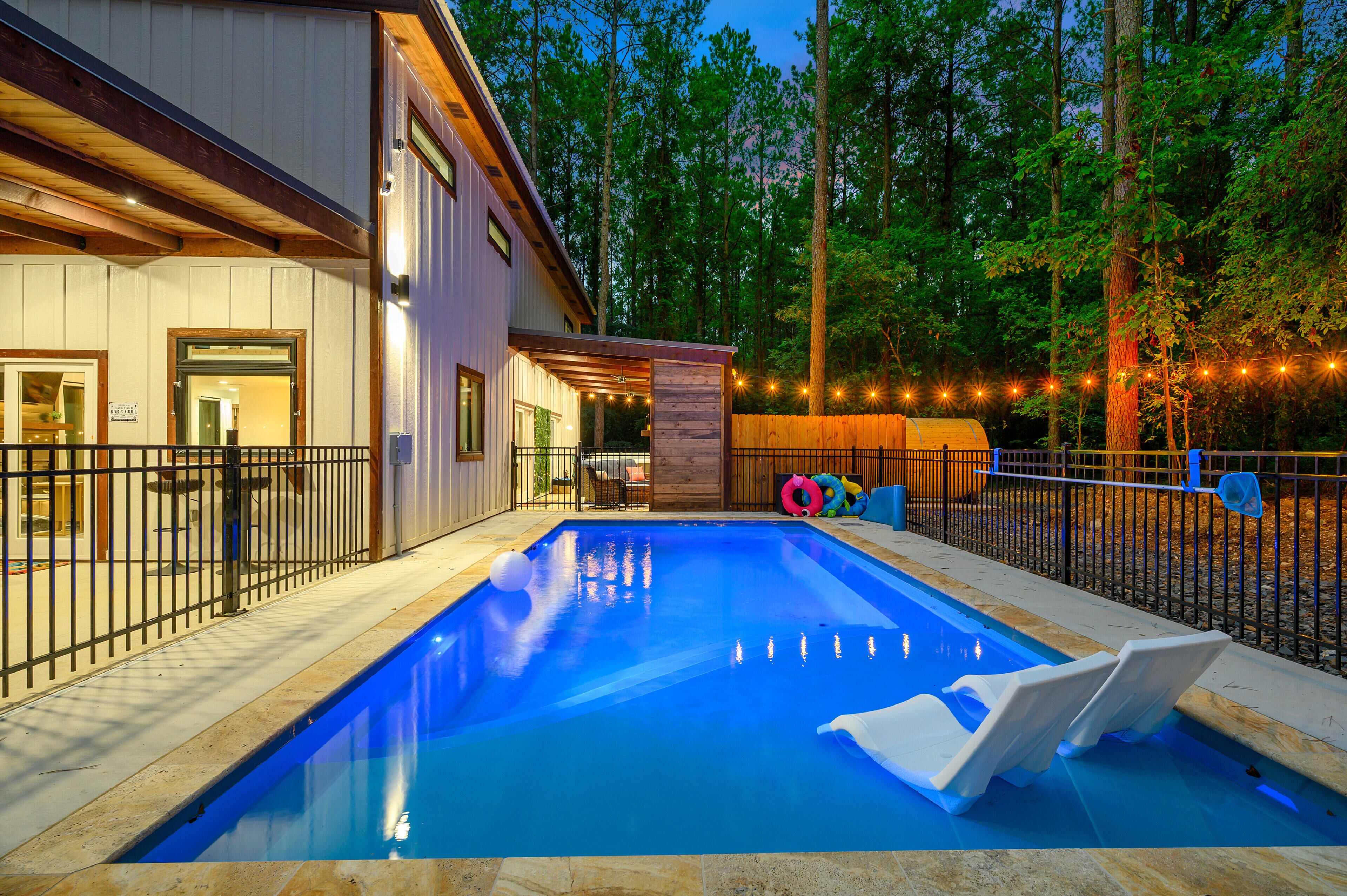 A swimming pool with a wooden deck, a fenced area, and a building with large windows.