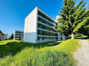 Ein mehrstöckiges Gebäude mit flachem Dach, umgeben von viel Grün und einem klaren Himmel.