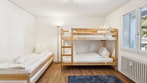 Een slaapkamer met stapelbed, een radiator, een raam met uitzicht en een vloerlamp.