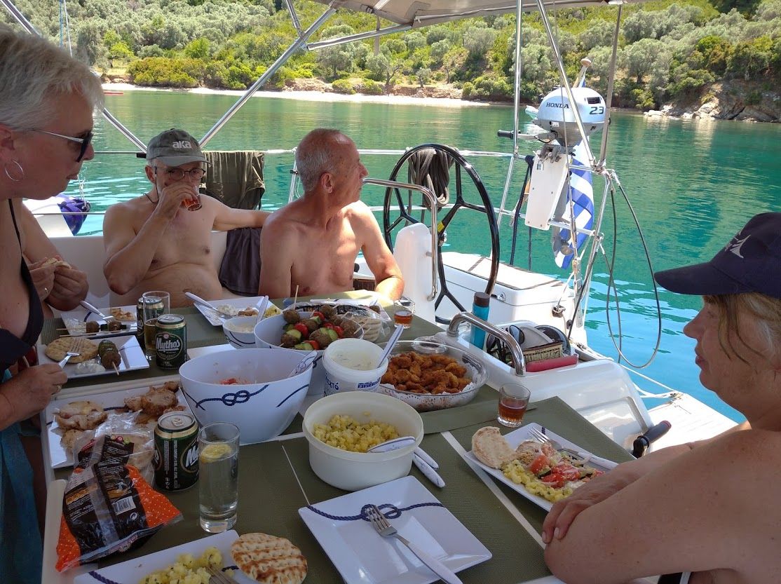 A boat with a dining table set with food and drinks, surrounded by people.