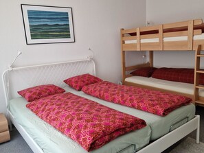 Ein Zimmer mit einem Etagenbett, zwei Einzelbetten, einem weißen Kopfende und einem gerahmten Bild an der Wand.