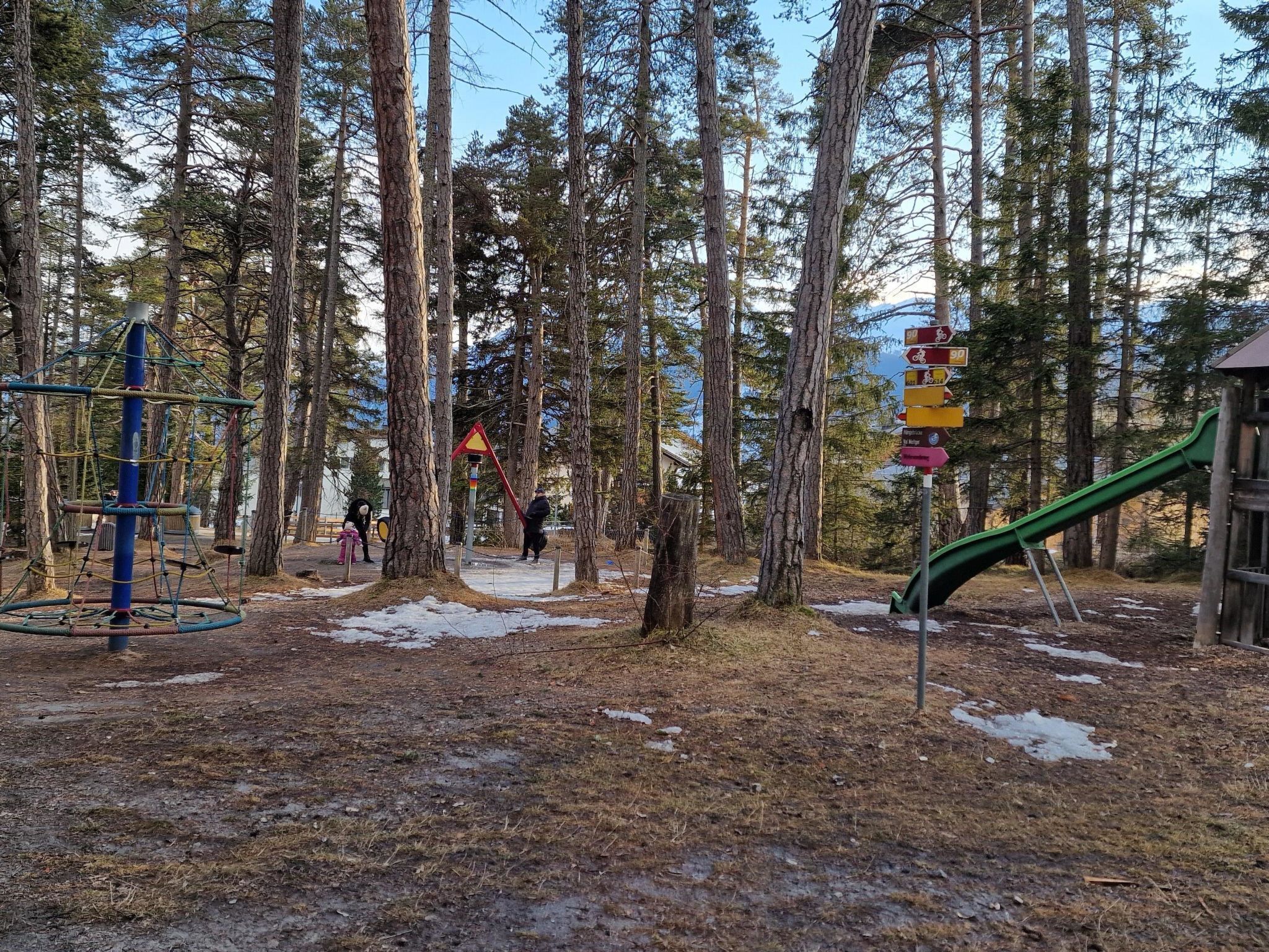 Ein Spielplatz mit einer Kletterkonstruktion, einer Rutsche und einem Wegweiser mit Richtungshinweisen.