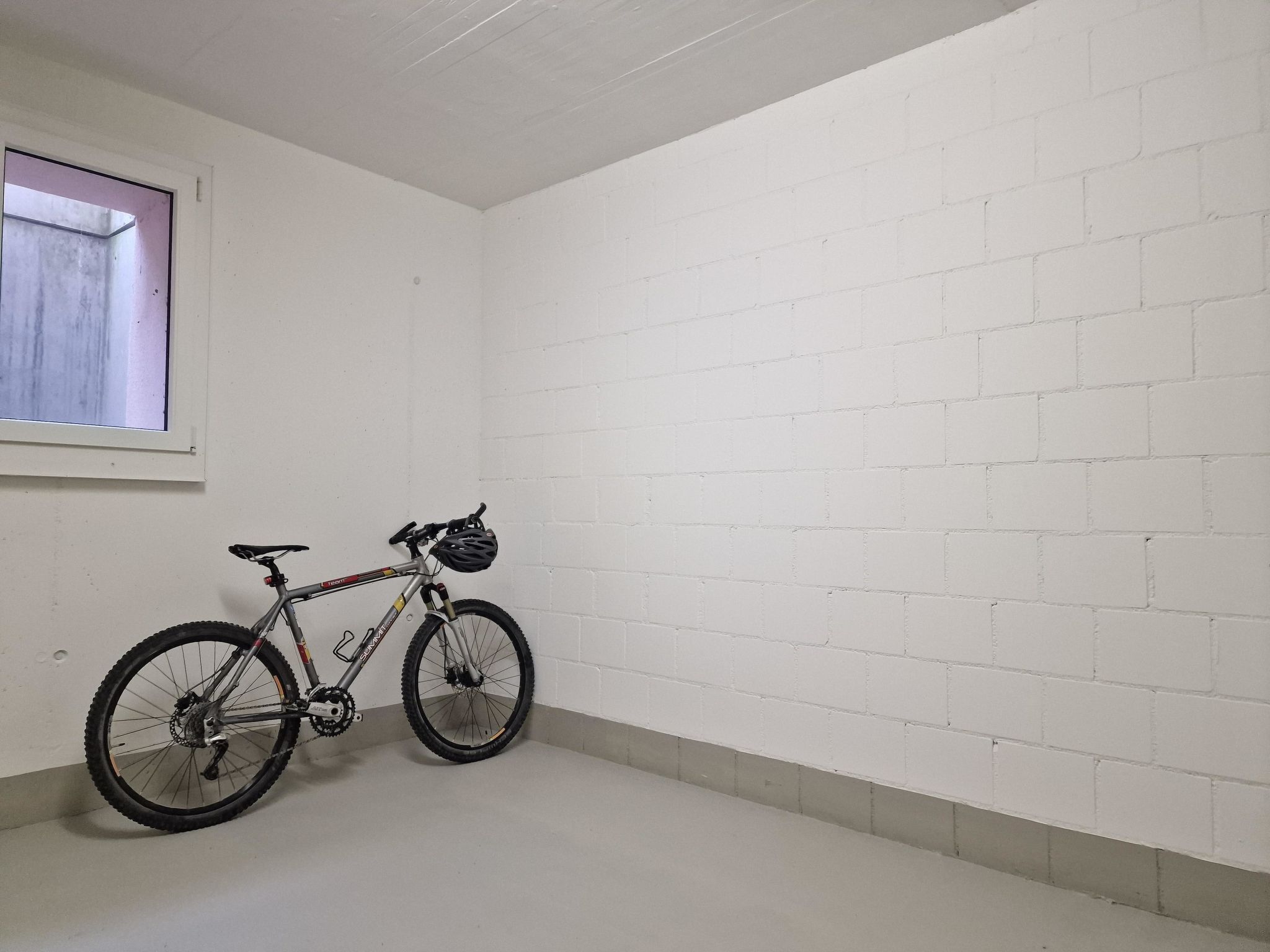 A room with white brick walls, a window with a view, and a bicycle leaning against the wall.