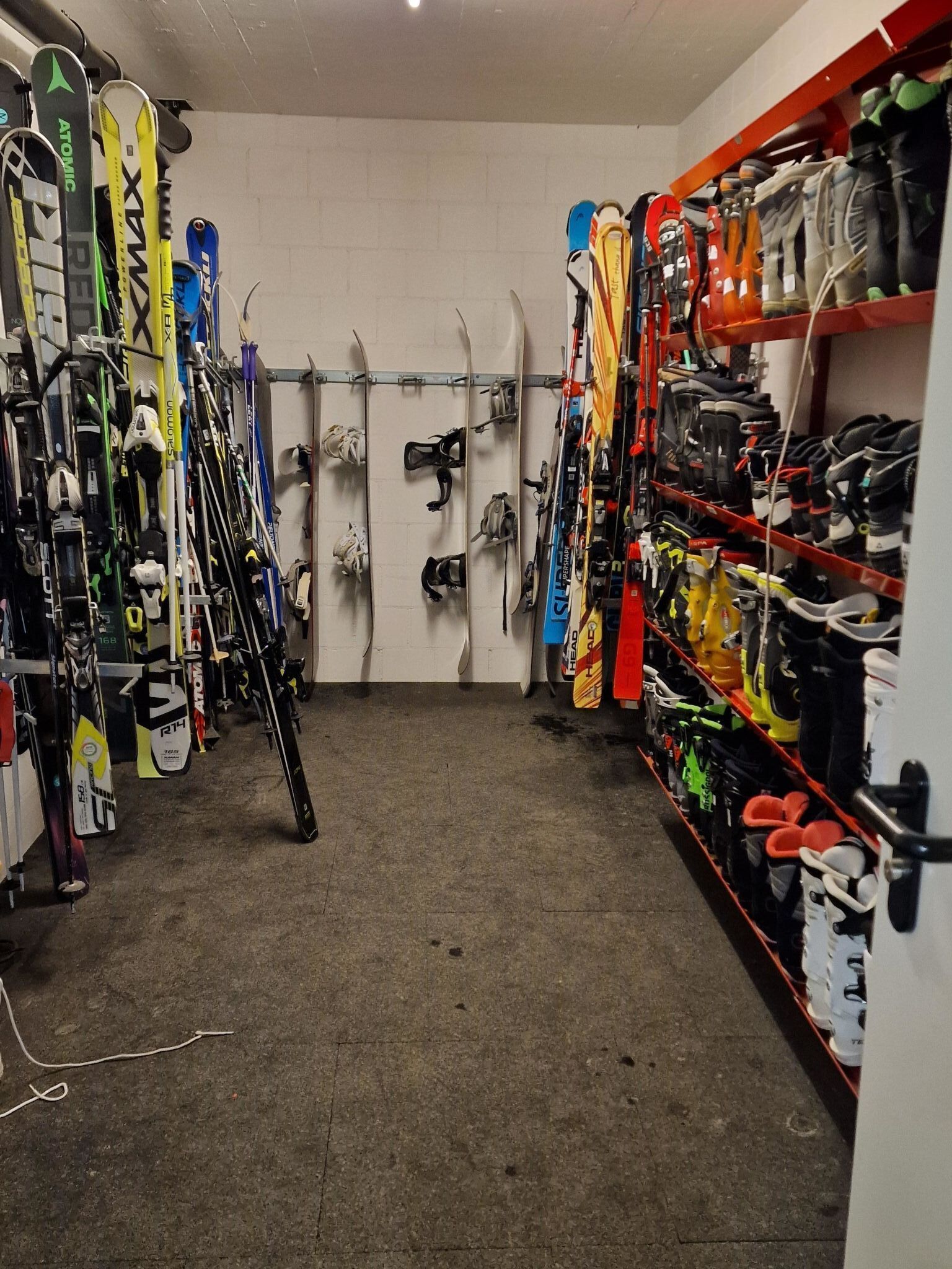 A ski equipment storage room with skis and ski boots organized on racks.