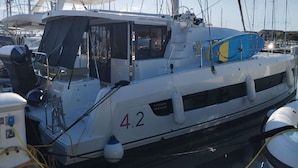 Een boot genaamd 'BALI 42' afgemeerd in een jachthaven, met andere boten, een hut met ramen en een blauwe reddingsboei op het dek.
