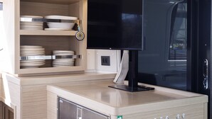 Eine kompakte Küche mit integrierten Geräten, darunter ein Kühlschrank und eine Mikrowelle, sowie ein Flachbildfernseher, der über der Arbeitsplatte angebracht ist.