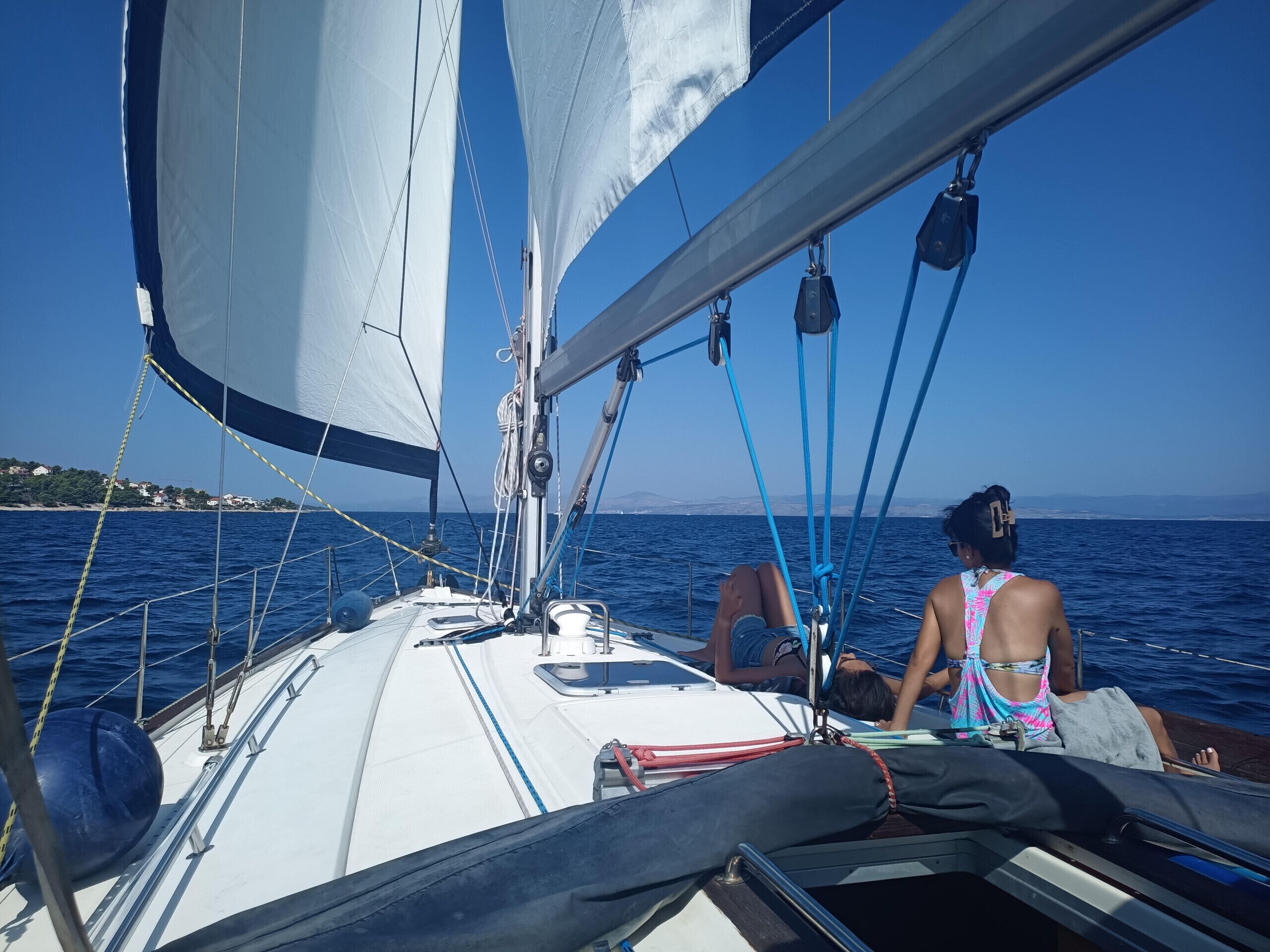 Een zeilboot met iemand op het dek, touwen en een helder uitzicht over de zee.