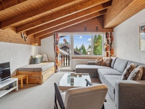 A cozy living room with a wooden ceiling, a sofa, a TV, and a window with a view of trees. - A301 Appartement/Fewo,   Ferienwohnung A301 by Interhome (Lenzerheide)