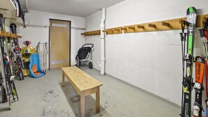 Et skiopbevaringsrum med en træbænk, ski og en klapvogn.