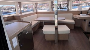 A boat interior with a kitchen area, seating, and large windows offering views of the marina.