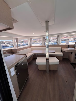 A boat interior with a kitchen area, seating, and large windows offering views of the marina.