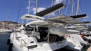 A white yacht docked at a marina with multiple masts and a clear blue sky.
