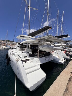 A white yacht docked at a marina with multiple masts and a clear blue sky.
