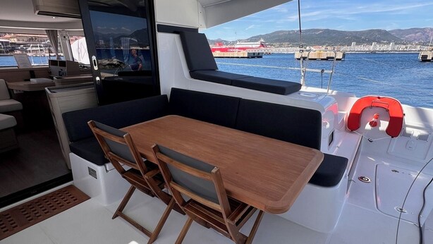 A boat's interior with a dining area, a TV screen, and a view of the harbor.