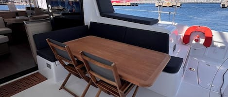 A boat's interior with a dining area, a TV screen, and a view of the harbor.