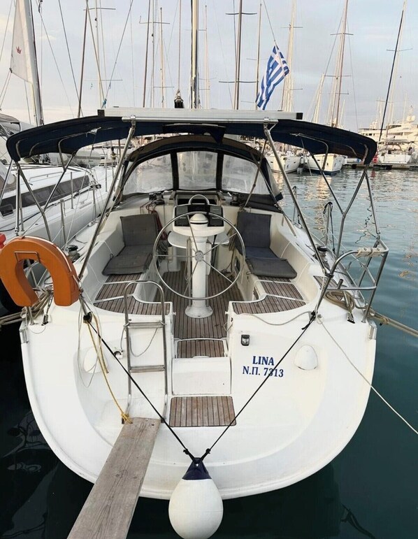 Eine Segelyacht liegt in einer Marina festgemacht, mit Pantry, Steuerrad und einem Namensschild mit der Aufschrift 'LINA N.P. 7313'.