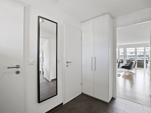Un pasillo con un espejo, un armario y una puerta que da a una habitación con una silla y vistas al exterior.