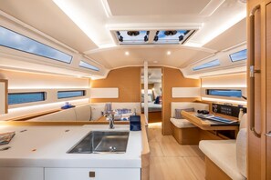 A yacht interior with a central dining area, a kitchen with a sink, and a seating area with a control panel.