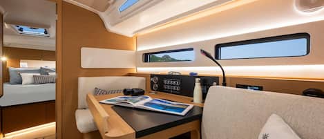 A compact, well-lit interior with a bed, a table with a magazine, a window, and a control panel.