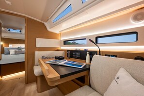 A compact, well-lit interior with a bed, a table with a magazine, a window, and a control panel.
