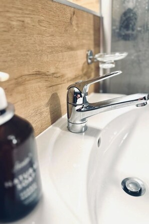 A bathroom sink with a chrome faucet, a wooden panel above, and a bottle of hand soap. - Steil Alva Studios Smit Studio, 0002 Steil Alva Studio 2 by Interhome (Lenzerheide)