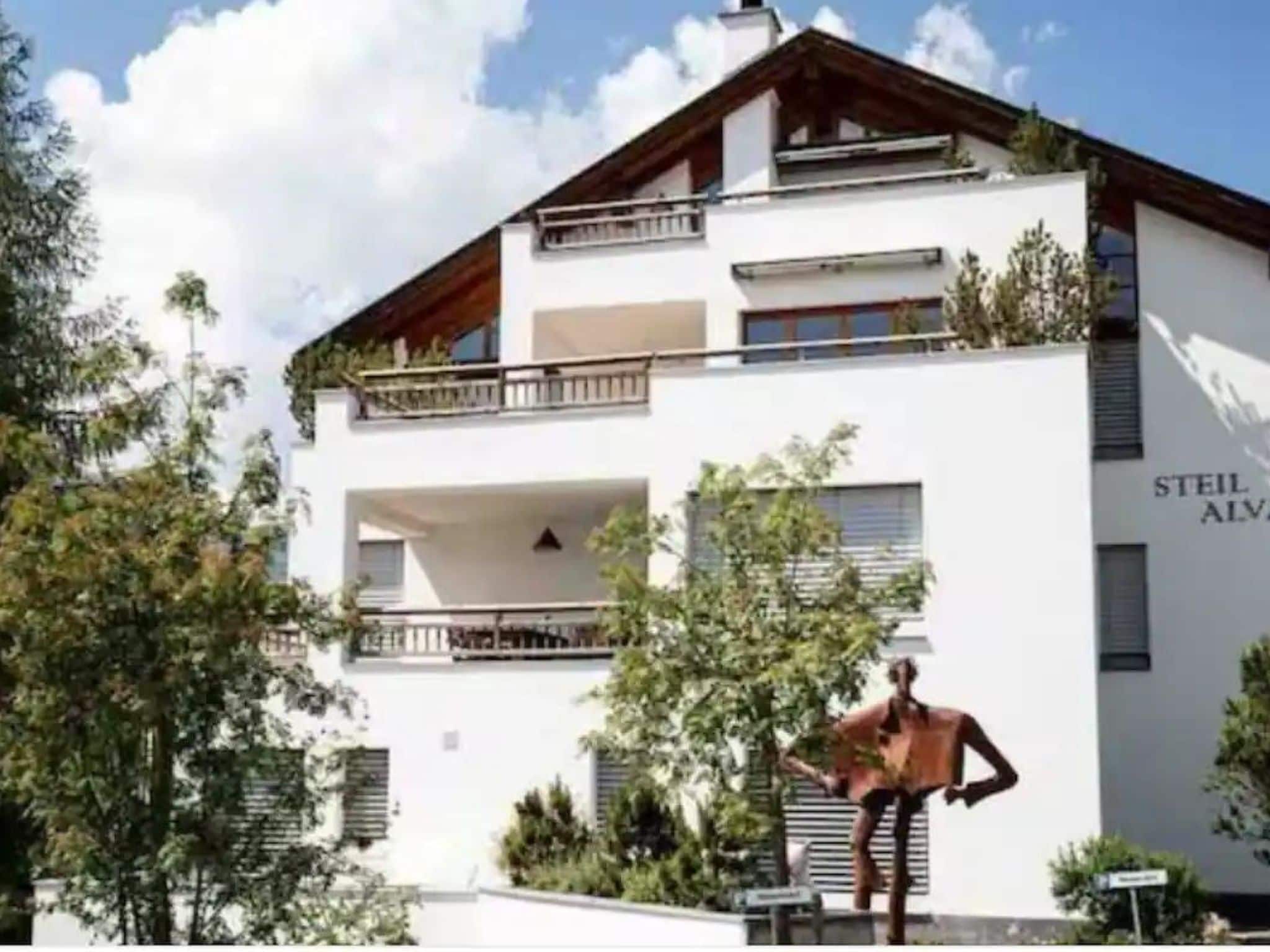 A two-story building with a white facade, balconies, and a sculpture of a person.