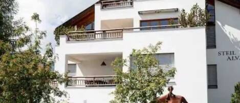 A two-story building with a white facade, balconies, and a sculpture of a person.