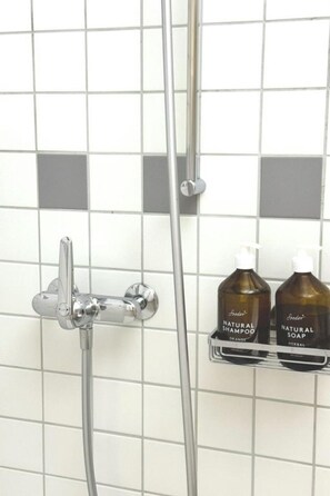 A shower area with a chrome faucet and a handheld showerhead. There are two bottles of natural shampoo and soap on a shelf. - Steil Alva Studios Smit Studio, 0002 Steil Alva Studio 2 by Interhome (Lenzerheide)