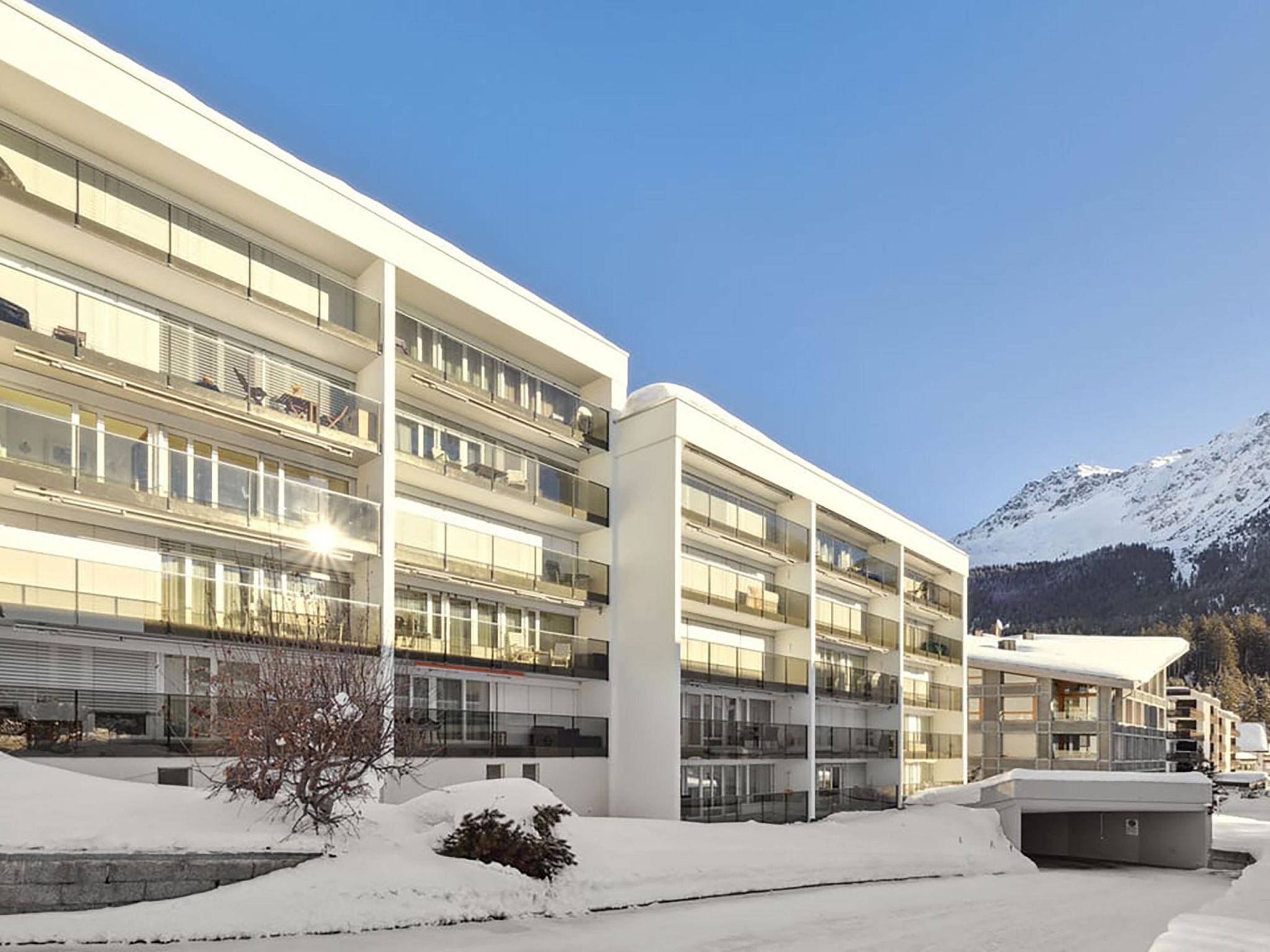 A modern multi-story building with large windows and balconies, surrounded by snow and mountains.
