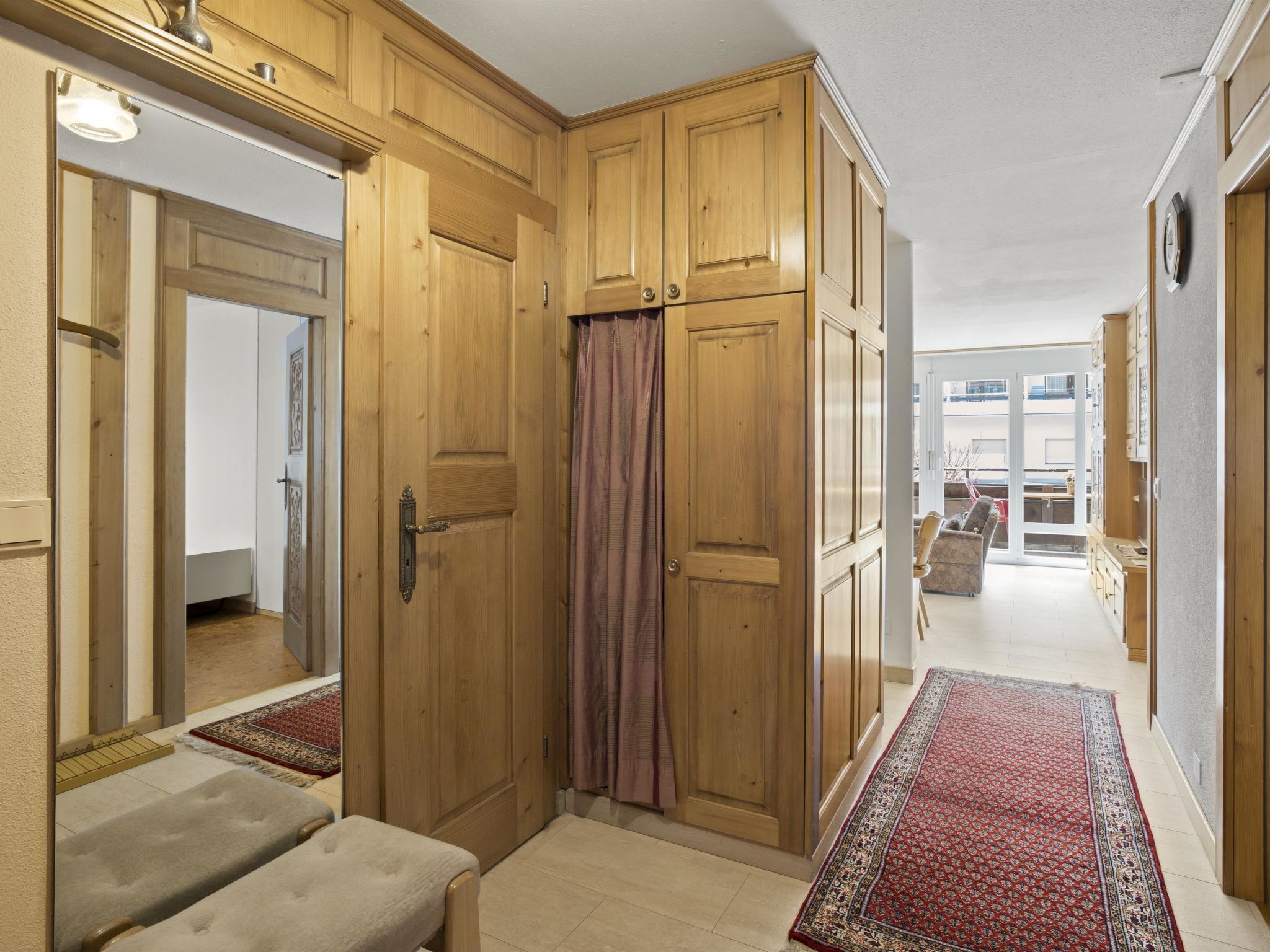 A hallway with wooden cabinets, a mirror, and a red patterned rug.