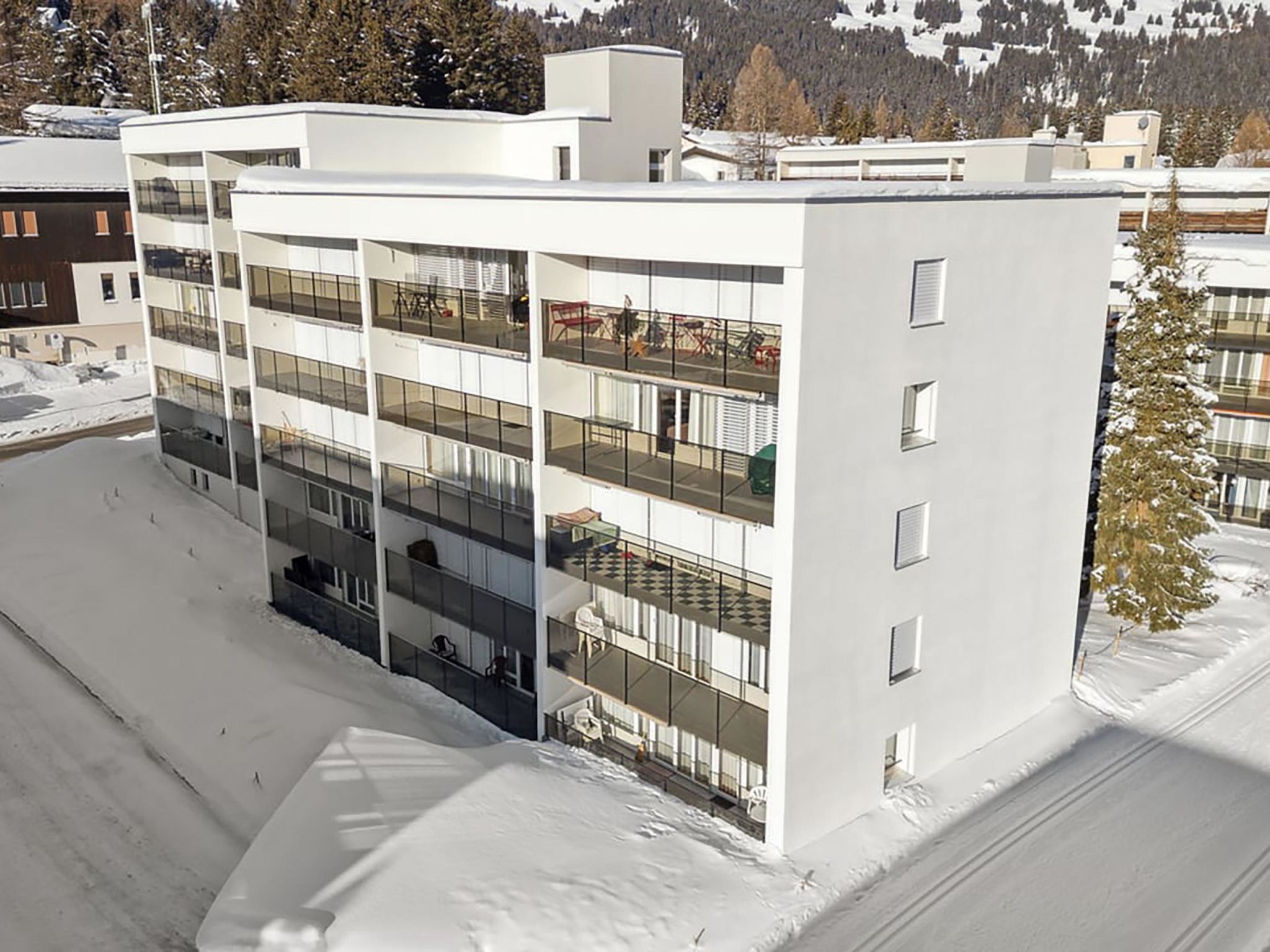 A modern multi-story building with balconies, surrounded by snow.