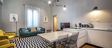 A modern kitchen with a dining area, a sofa, and a TV.