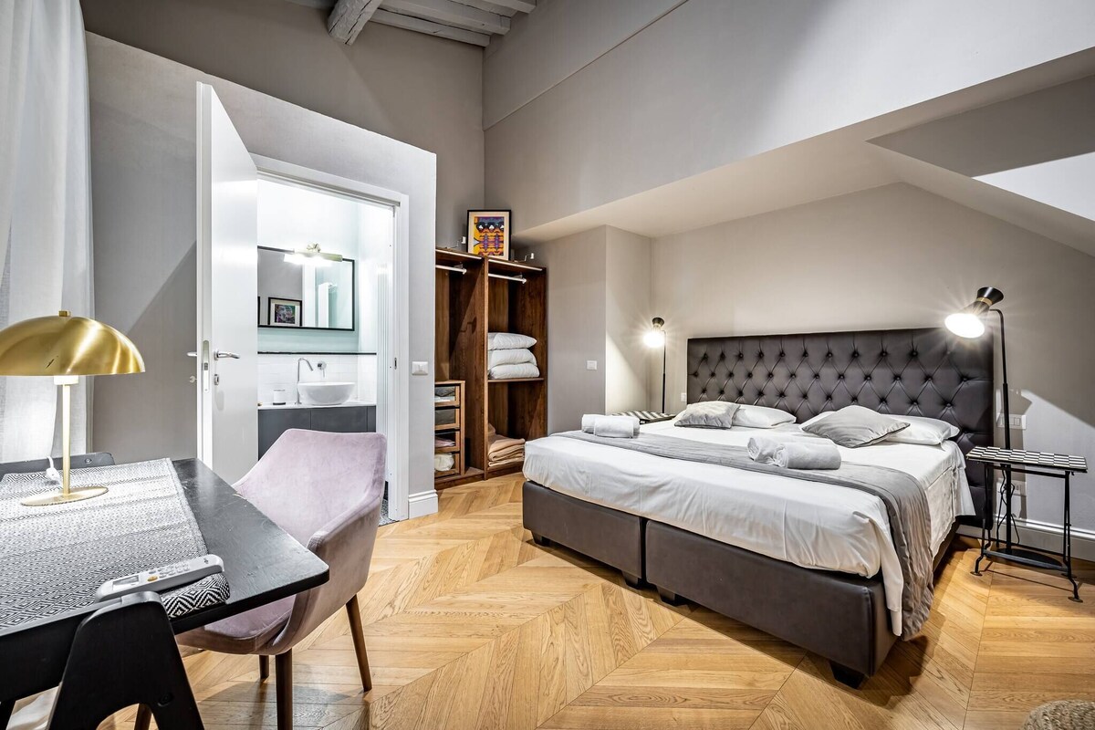 A modern bedroom with a large bed, bedside tables, a desk, and a wardrobe.