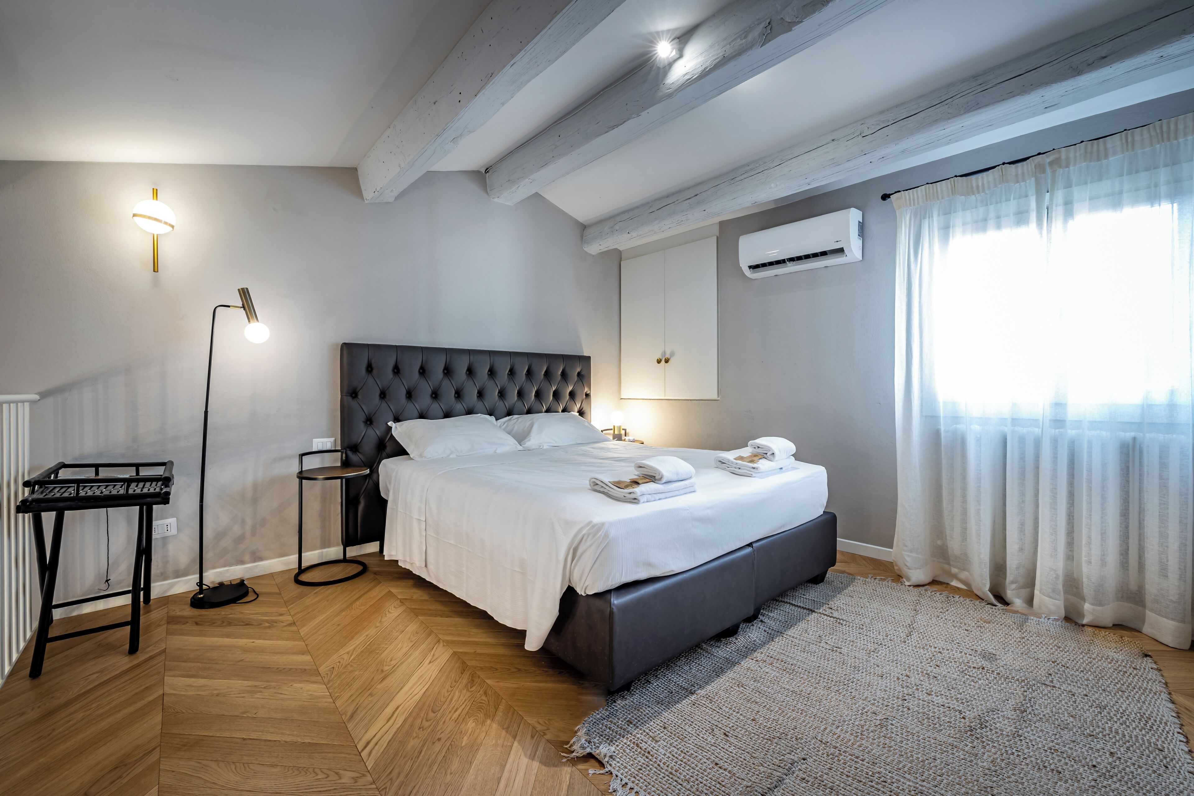 Une chambre à coucher comprenant un lit, des tables de chevet, une lampe, un appareil de climatisation et une fenêtre avec des rideaux.