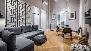 A modern living room with a grey sectional sofa, a herringbone-patterned wall, a dining area with a round table and chairs, and a visible air conditioning unit. - Ricasoli 29 n. 1 (Florence)