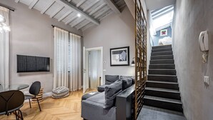 A modern living room with a grey sectional sofa, a wooden herringbone floor, a flat-screen TV, and a staircase leading to an upper level. - Ricasoli 29 n. 1 (Florence)