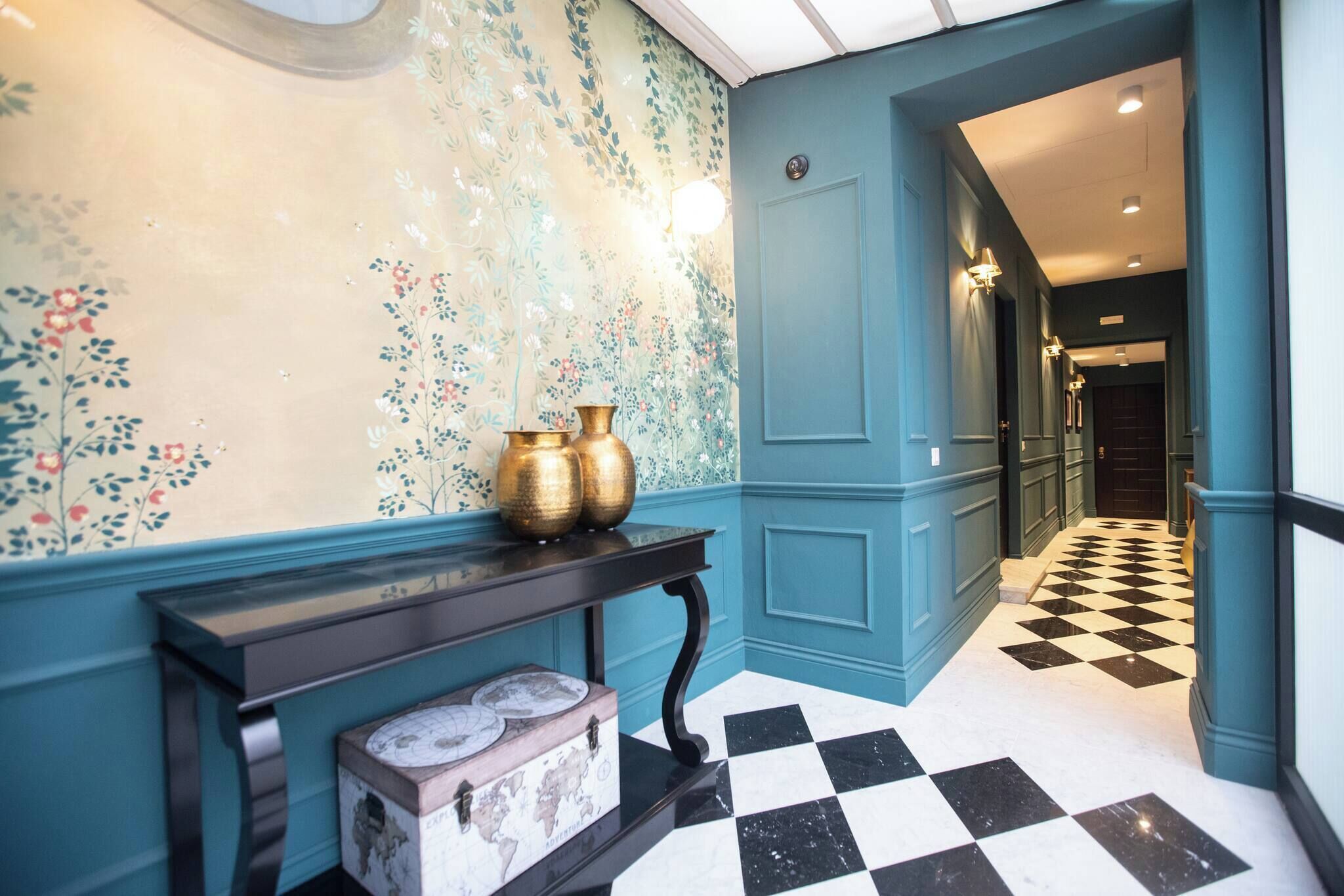 Un couloir aux murs de couleur turquoise, avec un sol à carreaux noirs et blancs et une console décorative agrémentée de vases.