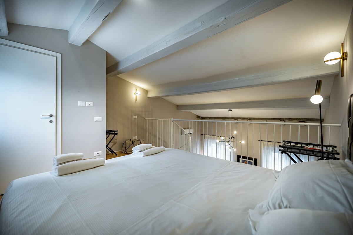 A bedroom with a large bed, a wardrobe, a staircase, and a view of the outdoors.