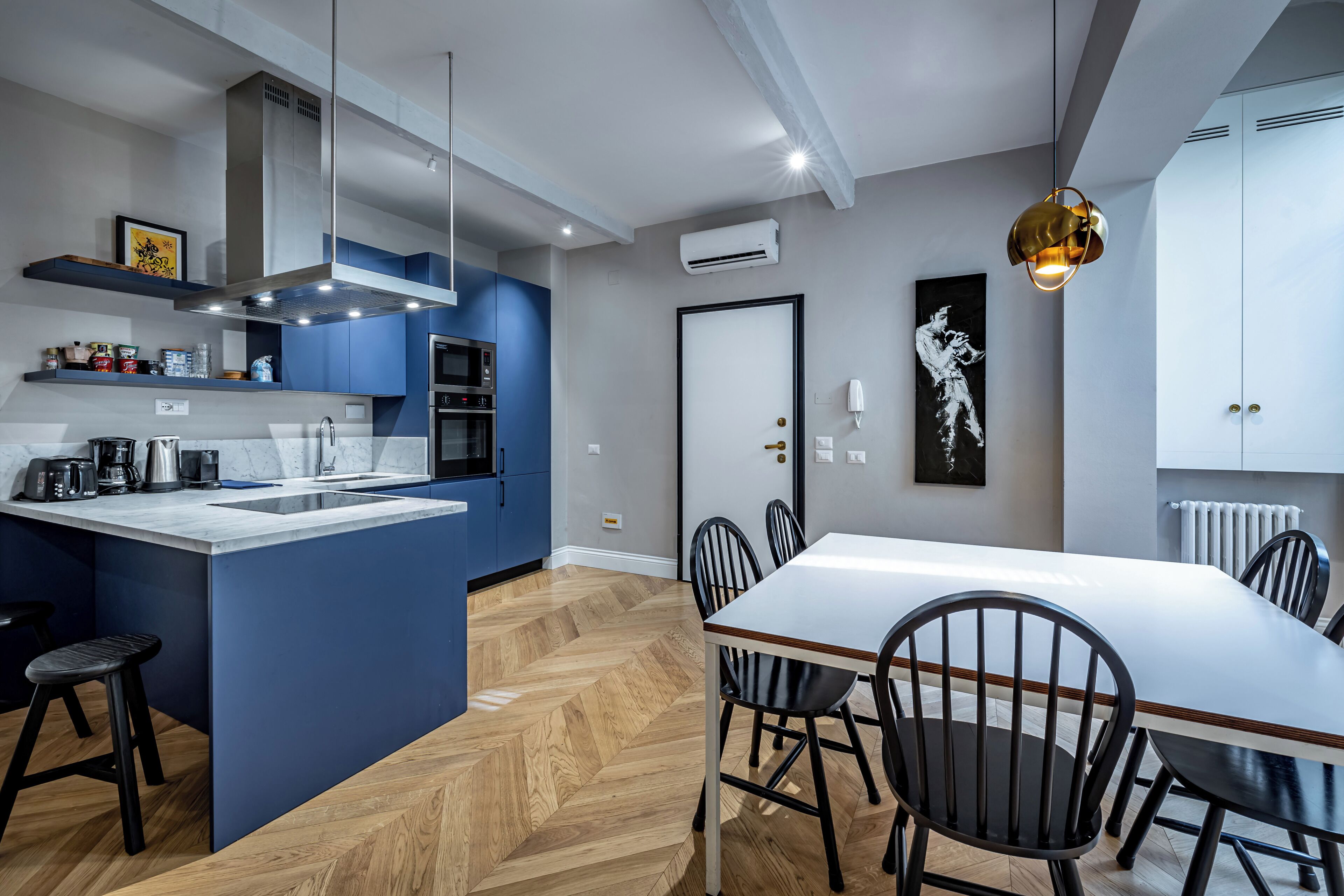 A modern kitchen with a central island, a dining area with a white table and black chairs, and a pendant light.