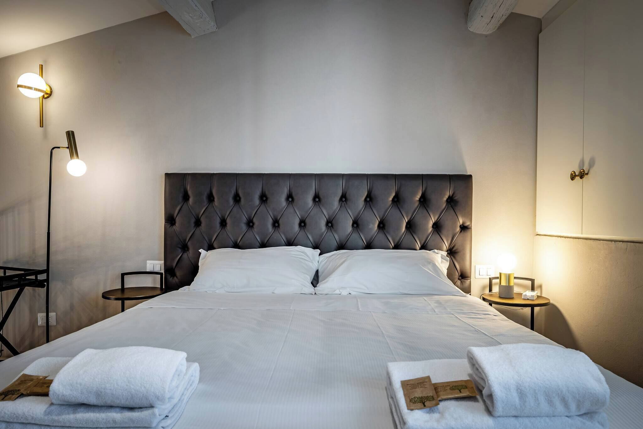 A neatly made bed with a tufted headboard, two bedside tables with lamps, and a wall-mounted light fixture.