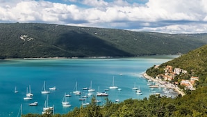 Uma cidade costeira com um porto cheio de veleiros, cercada por colinas e um céu claro.