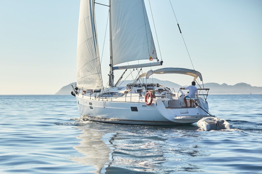 A sailboat with a person steering, a lifebuoy, and a calm sea with mountains in the background.